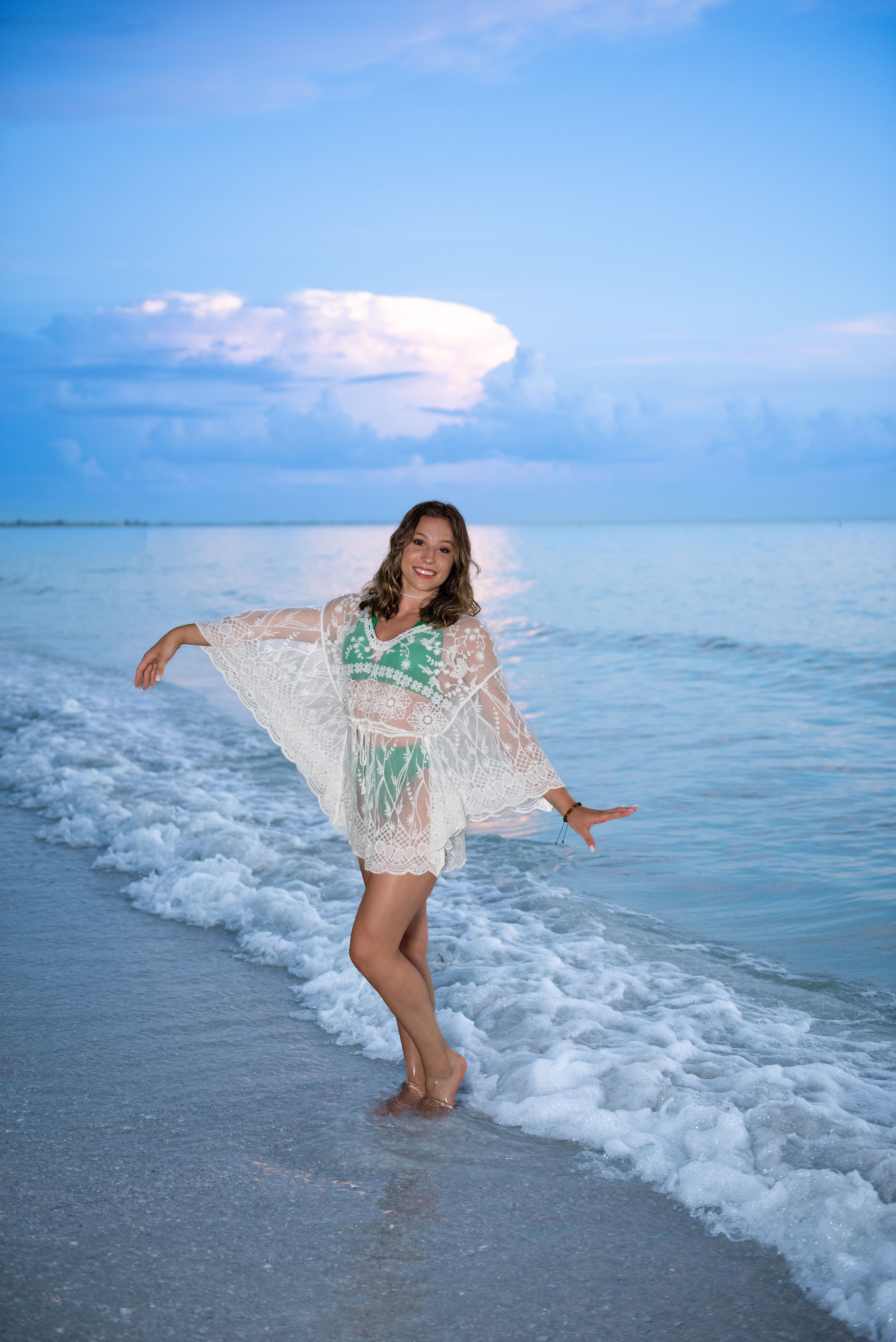 Senior in lace beach coverup dancing in Gulf of Mexico waves at sunset
